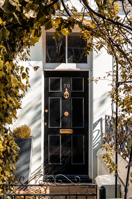 Close-up view of a black front door with the number 70 displayed in brass numerals, set within a white exterior wall. The door features decorative paneling and a brass door knocker shaped like a ring 